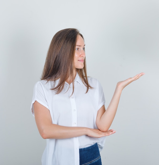 Junge Frau, die weg mit Handzeichen in weißem T-Shirt, Jeans schaut und froh schaut