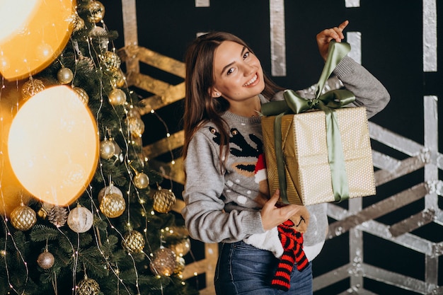 Junge Frau, die Weihnachtsgeschenk durch den Weihnachtsbaum auspackt