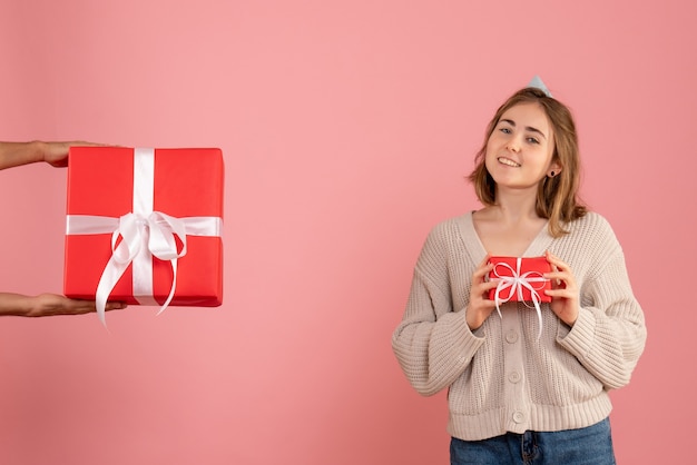 junge Frau, die Weihnachtsgeschenk hält und Geschenk vom Mann auf rosa annimmt