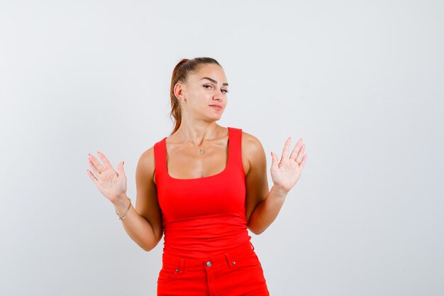 Junge Frau, die zehn Finger im roten Trägershirt, in der Hose und im misstrauischen Vorderansicht zeigt.