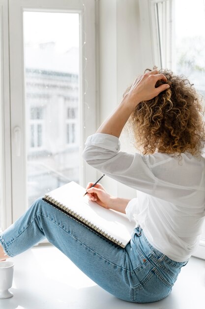 Junge Frau, die zu Hause nahe am Fenster zeichnet