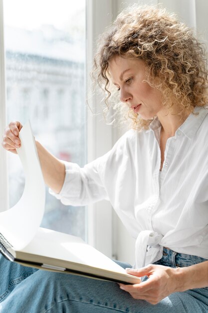 Junge Frau, die zu Hause nahe am Fenster zeichnet