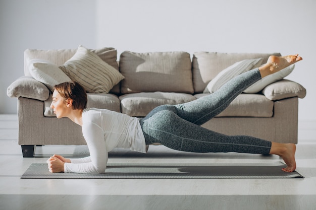 Junge Frau, die zu Hause Yoga auf Matte praktiziert