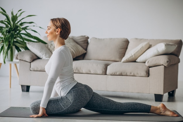 Junge Frau, die zu Hause Yoga auf Matte praktiziert