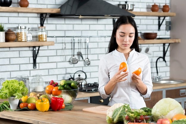 Junge Frau, die zu Hause zwei halbe Orangen in der Küche betrachtet
