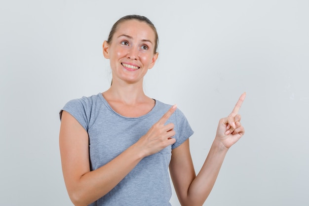 Junge Frau, die zur Seite im grauen T-Shirt zeigt und fröhlich, Vorderansicht schaut.