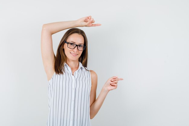 Junge Frau, die zur Seite im T-Shirt zeigt und fröhlich schaut. Vorderansicht.