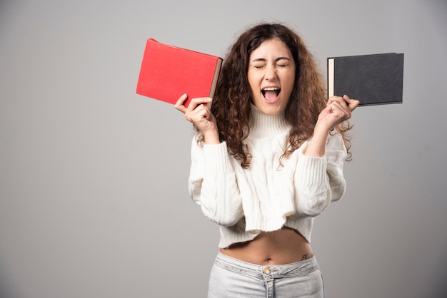 Junge Frau, die zwei Bücher an einer grauen Wand hält. Hochwertiges Foto