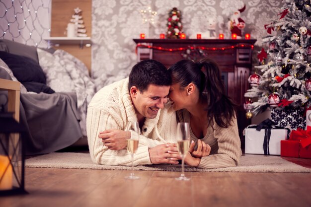 Junge Frau flüstert ihrem Ehemann etwas ins Ohr und feiert Weihnachten. Weihnachtsbaum