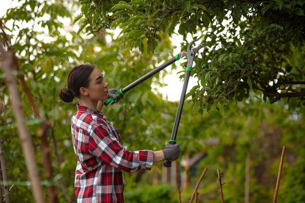 Junge Frau Gadener schneidet Äste am Baum und kümmert sich um Konzept des Naturhobbygartens