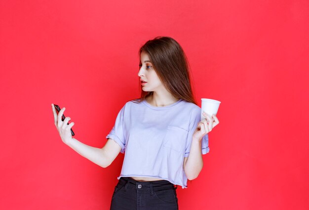 junge Frau hält eine Tasse Getränk und überprüft ihre Nachrichten.