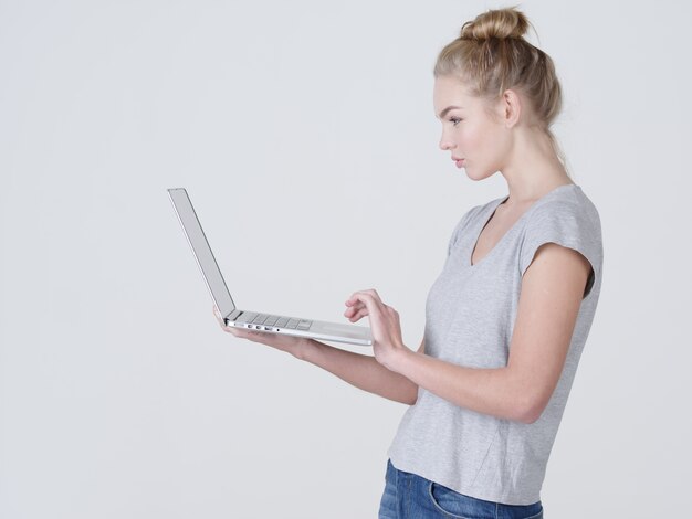 Junge Frau hält Laptop in Habds. Ruhiges kaukasisches Mädchen mit Notizbuch, das im Studio aufwirft