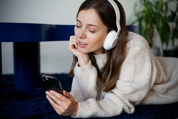 Junge Frau hört Musik mit ihrem Smartphone, während sie auf dem Boden liegt