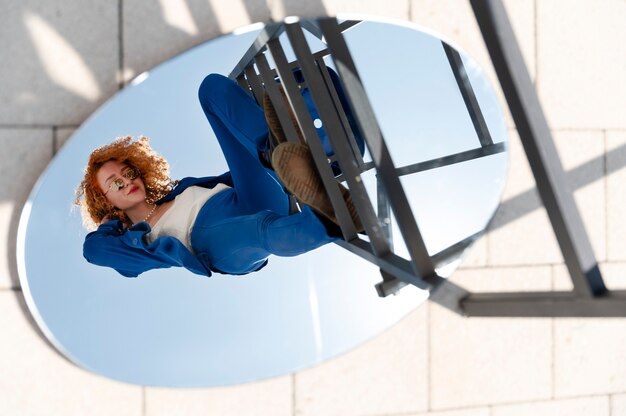 Junge Frau im blauen Anzug posiert mit Spiegel im Freien