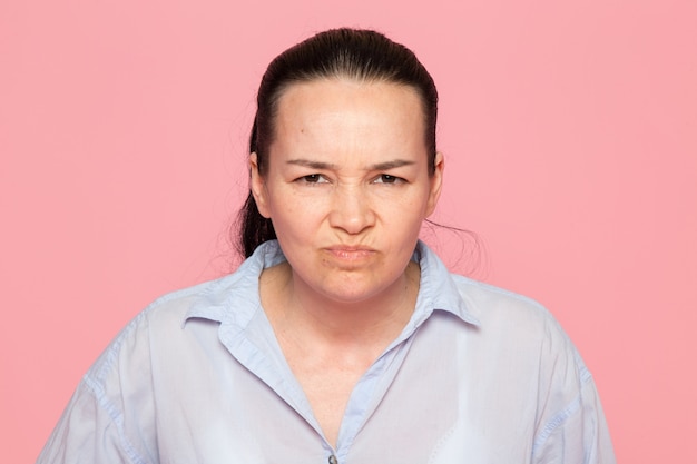 junge Frau im blauen Hemd, das auf der rosa Wand aufwirft