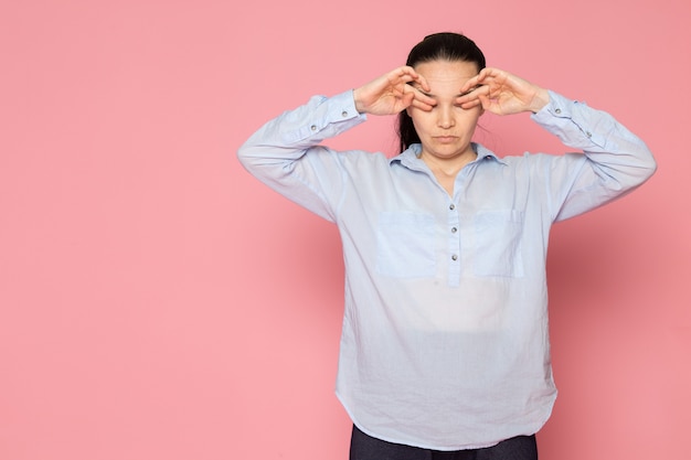 junge Frau im blauen Hemd, das auf der rosa Wand aufwirft