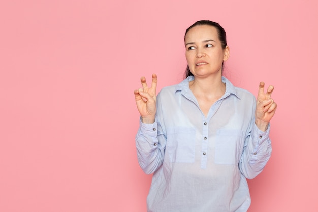 junge Frau im blauen Hemd, das auf der rosa Wand aufwirft