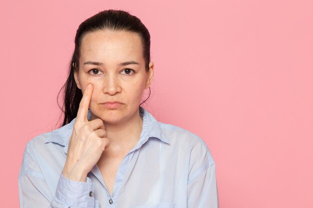 junge Frau im blauen Hemd, das auf der rosa Wand aufwirft