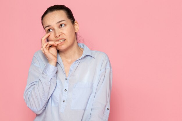 junge Frau im blauen Hemd, das auf der rosa Wand aufwirft