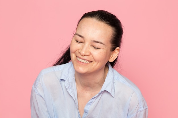 Kostenloses Foto junge frau im blauen hemd, das auf der rosa wand aufwirft