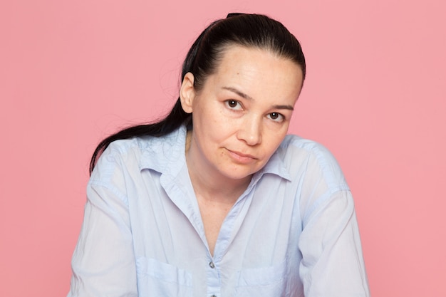 junge Frau im blauen Hemd, das auf der rosa Wand aufwirft