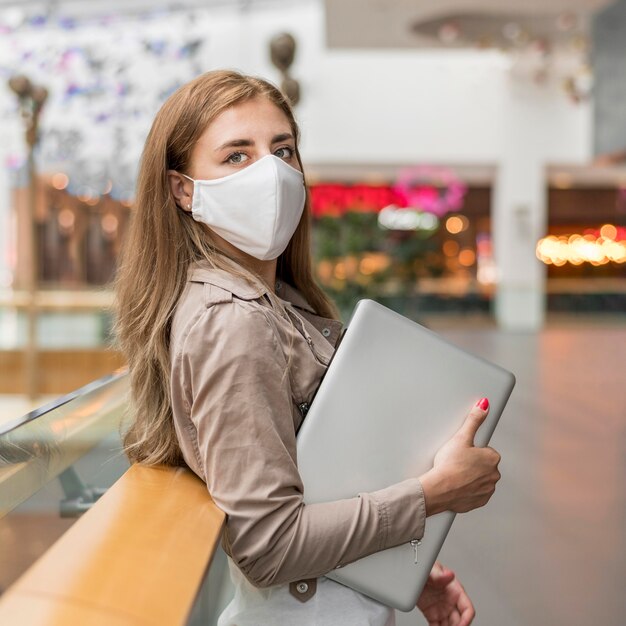 Junge Frau im Einkaufszentrum mit Laptop, die Maske trägt