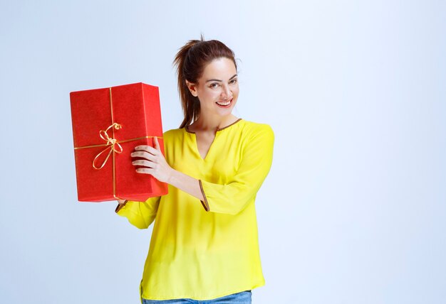 Junge Frau im gelben Hemd hält eine rote Geschenkbox am Valentinstag