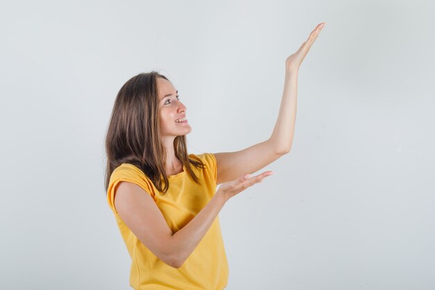 Junge Frau im gelben T-Shirt, das Arme hält, wie etwas erhöhen.