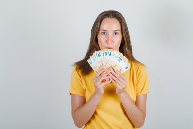 Junge Frau im gelben T-Shirt, Euro-Banknoten haltend und vorsichtig aussehend