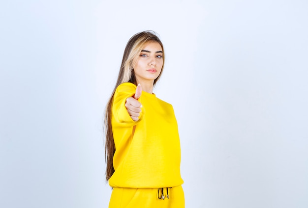 Junge Frau im gelben Trainingsanzug posiert vor der Kamera über der weißen Wand