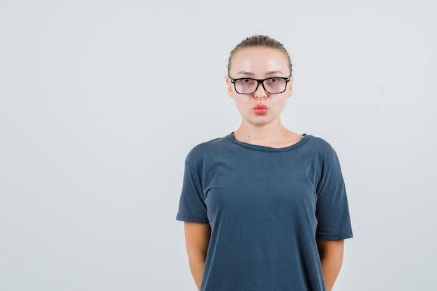 Junge Frau im grauen T-Shirt, Brille, die Lippen gefaltet hält und klug aussieht