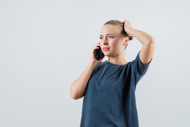 Junge Frau im grauen T-Shirt, das auf Handy spricht und enttäuscht schaut
