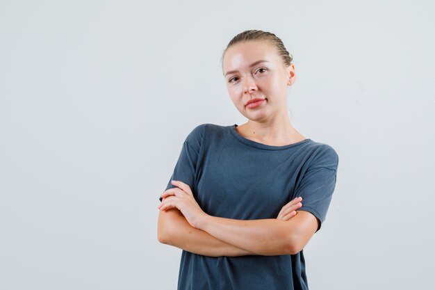 Junge Frau im grauen T-Shirt, das mit verschränkten Armen steht und zuversichtlich schaut