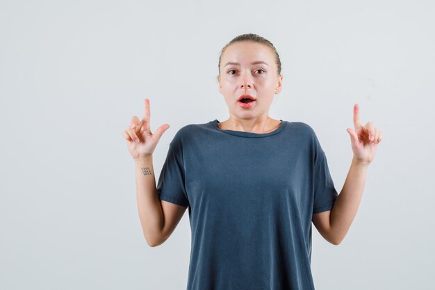 Junge Frau im grauen T-Shirt, das oben zeigt und verwirrt schaut