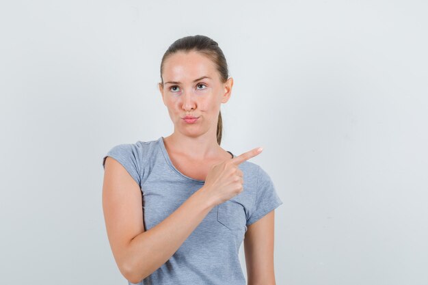 Junge Frau im grauen T-Shirt, das zur Seite zeigt und nachdenklich, Vorderansicht schaut.