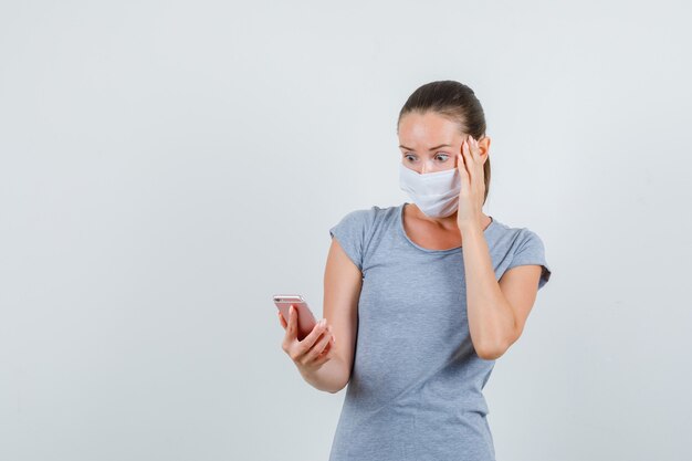 Junge Frau im grauen T-Shirt, Maske und schaut überrascht. Vorderansicht.