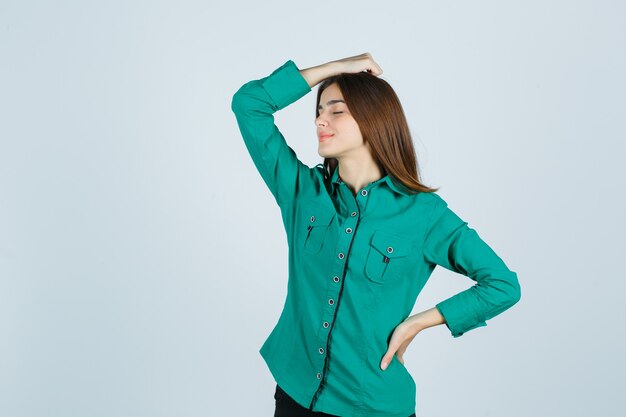 Junge Frau im grünen Hemd, das Hand auf Kopf hält und entspannt, Vorderansicht schaut.