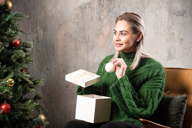 Junge Frau im grünen warmen Pullover sitzend und posierend mit einer Geschenkbox