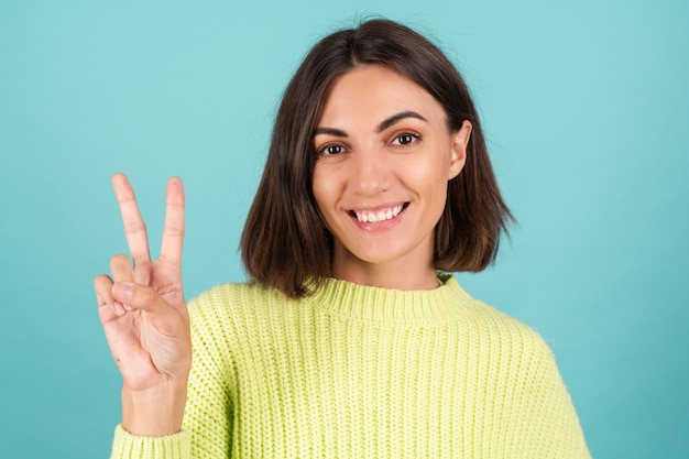 Junge Frau im hellgrünen Pullover lächelnd zeigt V-Zeichen
