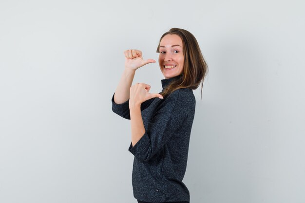 Junge Frau im Hemd, das mit Daumen weg zeigt und positiv schaut.