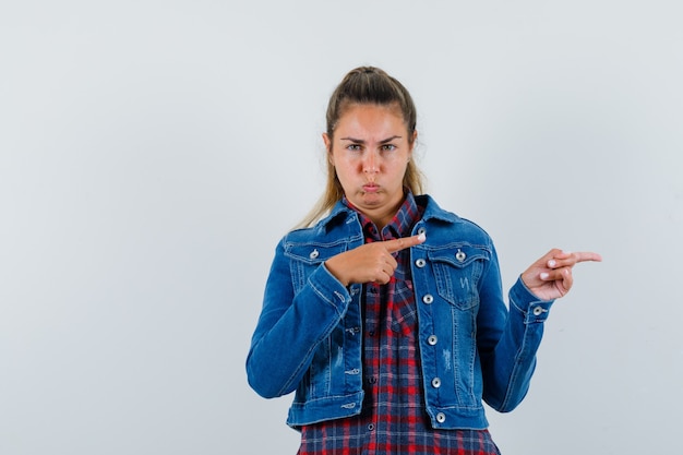 Junge Frau im Hemd, Jacke, die zur Seite zeigt und boshaft schaut, Vorderansicht.