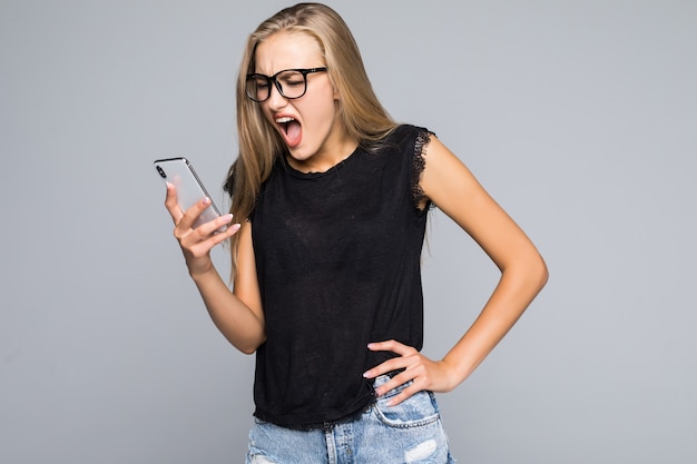 Junge frau im hemd schreit am telefon lokalisierten grauen hintergrund