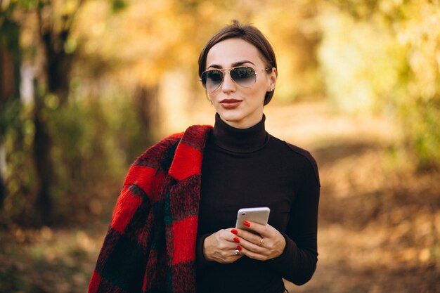 Junge Frau im Herbstpark unter Verwendung des Telefons