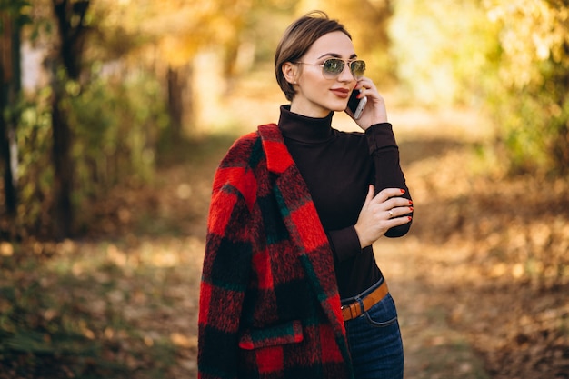 Junge Frau im Herbstpark unter Verwendung des Telefons