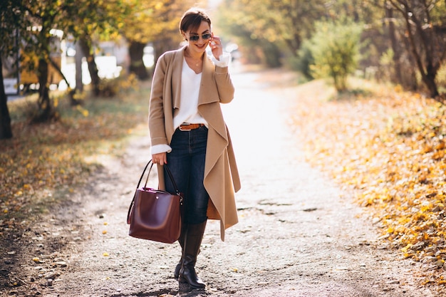 Junge Frau im Herbstpark unter Verwendung des Telefons