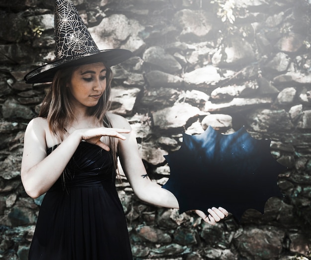 Junge Frau im Hexenhut, der Magie mit Halloween-Dekoration zeigt