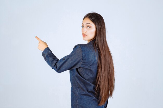 Junge Frau im Jeanshemd, das auf etwas hinter zeigt