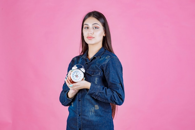 Junge Frau im Jeanshemd, das den Wecker zwischen ihren Händen hält