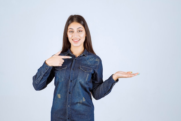 Junge Frau im Jeanshemd, das etwas in ihrer Hand zeigt