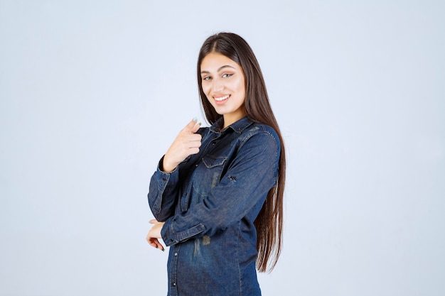 Junge Frau im Jeanshemd, die jemanden nach vorne zeigt und ihn einlädt